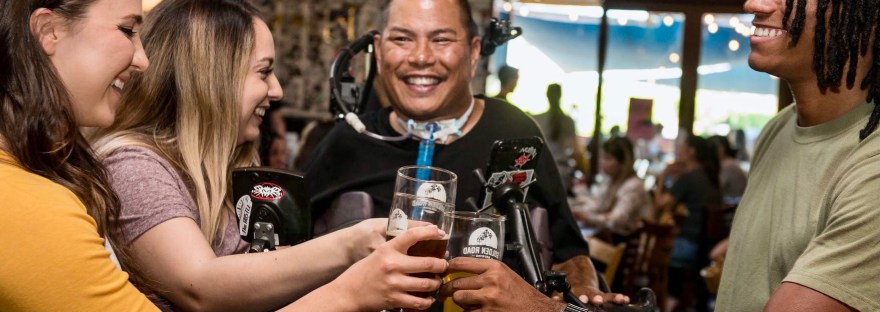 Een vrolijke groep mensen met en zonder beperking die proosten in een cafe.