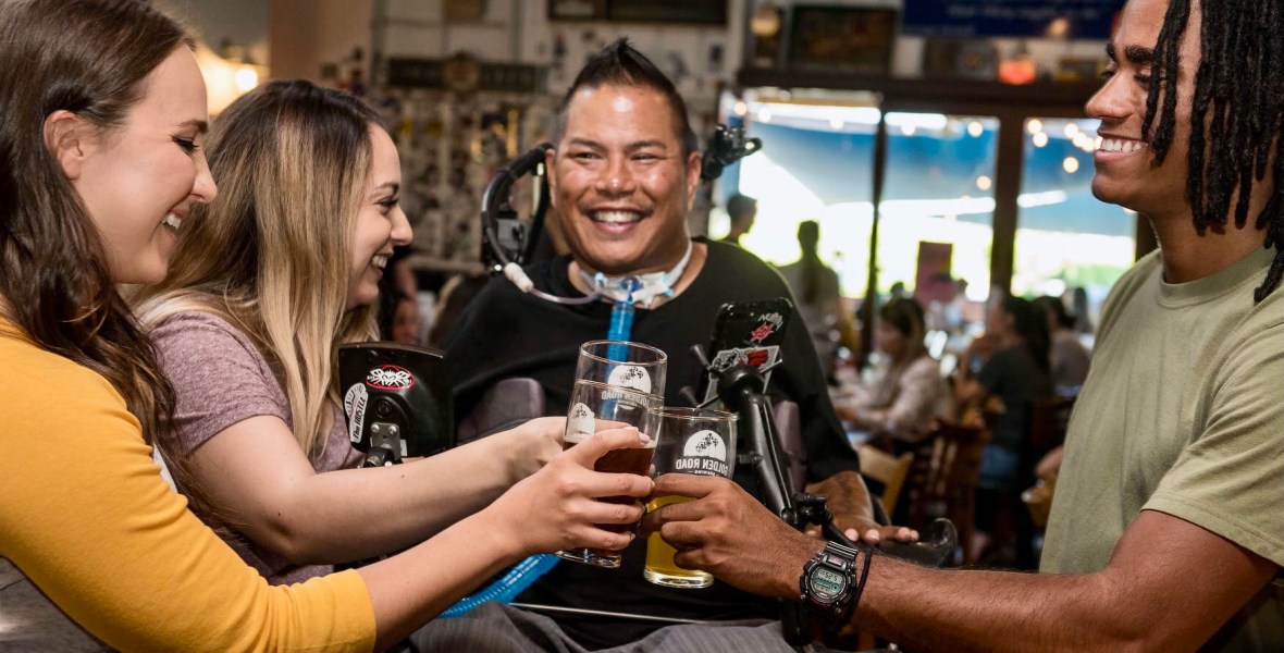 Een vrolijke groep mensen met en zonder beperking die proosten in een cafe.