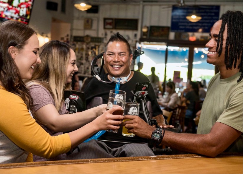 Een vrolijke groep mensen met en zonder beperking die proosten in een cafe.