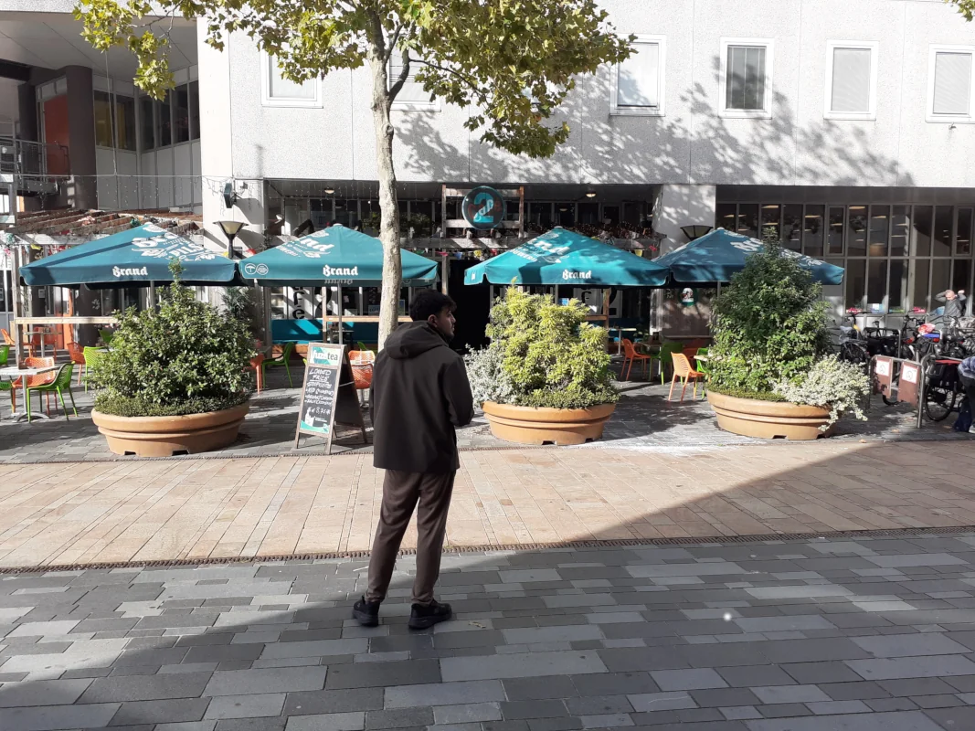 Het terras en de ingang van Café op 2 aan het Stadhuisplein in Almere. Er staan groene parasols en grote plantenbakken voor de deur.