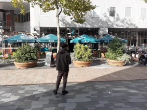 Het terras en de ingang van Café op 2 aan het Stadhuisplein in Almere. Er staan groene parasols en grote plantenbakken voor de deur.